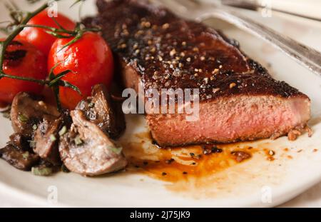 New York Streifensteak mit gebratenen Pilzen und Tomaten Stockfoto