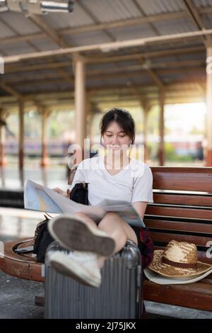 Glückliche junge asiatische Frau Reisende oder Backpacker mit Karte wählen, wo mit Gepäck am Bahnhof zu reisen, Sommerurlaub Reisekonzept Stockfoto