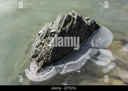 Ein Felsbrocken, umgeben von Eis, inmitten eines gefrorenen Sees in der Nähe des Himalaya-Gebirgspass von Shingo La in Zanskar in Indien. Stockfoto