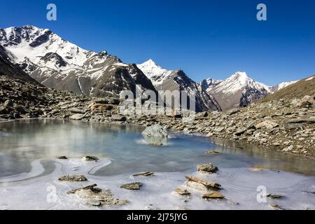 Ein gefrorener See mit Blick auf schneebedeckte Himalaya-Gipfel auf einer Höhenwanderung zum Shingo La Pass in der Zanskar-Region im indischen Himalaya. Stockfoto