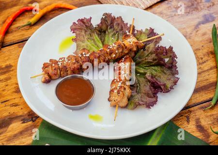 asiatischer Kebab im tropischen Stil auf dem Teller mit Bananen- und Salatblättern und Sesamsamen auf dem Holztisch Stockfoto