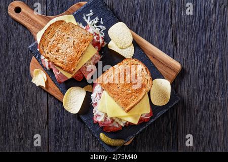 amerikanisches reuben-Sandwich mit Roggenbrot in dünne Scheiben geschnittenes Corned Beef, Sauerkraut, russischem Dressing und geschmolzenem Käse an Bord mit Kartoffelchips im Dunkeln Stockfoto