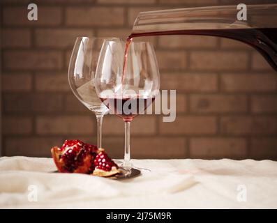 Rotwein, der aus einem Dekanter in ein Glas gießt; Granatapfel Stockfoto