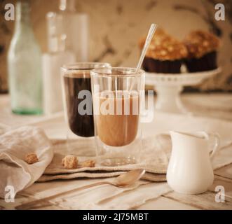 Schwarzer Kaffee und Kaffee mit Milch; Frühstücksmuffins im Hintergrund Stockfoto