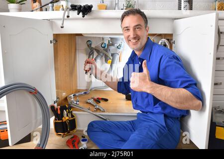 Klempner reparieren Leck in Waschbecken eines Hauses mit Werkzeugen um lächelnd mit der Hand und ok Geste. Horizontale Zusammensetzung. Stockfoto
