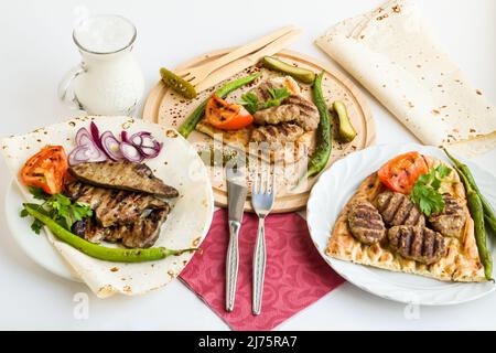 Gegrillt, Fleischbällchen und Lebersteak, entworfen mit Gemüse und türkischem Fladenbrot auf hölzernen Serviertellern Stockfoto