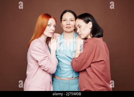 Liebevolle multiethnische Töchter umarmen Mutter vor braunem Hintergrund Stockfoto
