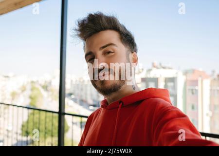 Posiert, junger Mann, der Selfie macht, bärtiger Erwachsener, in rotem Sweatshirt gekleidet Stockfoto