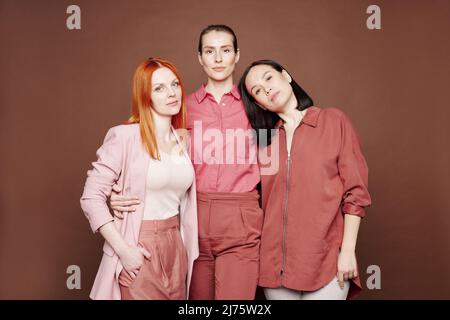 Gruppe moderner junger multiethnischer Frauen, die vor braunem Hintergrund posieren Stockfoto