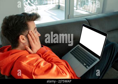 Der junge Erwachsene ist schockiert über das, was er auf dem Laptop sieht, Laptop mit leerem weißen Bildschirm und Text, der zur Platzierung bereit ist Stockfoto