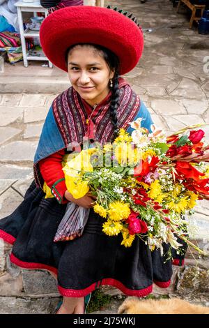 Ein Porträt einer jungen indigenen Quechua-Frau, die Blumen auf dem Sonntagsmarkt im Dorf Chinchero, Region Cusco, Peru, hält. Stockfoto