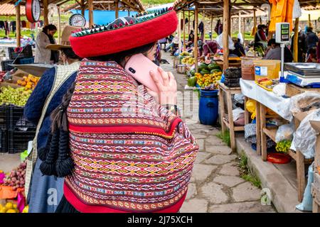 Eine junge indigene Quechua-Frau, die Mobiltelefone auf dem berühmten Sonntagsmarkt im Dorf Chinchero, Region Cusco, Provinz, Peru benutzt. Stockfoto