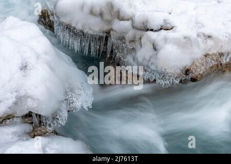 Eiszapfen hängen über dem klaren Wasser des Rissbaches in Tirol an einem schmalen Punkt bei Hinterriss. Stockfoto