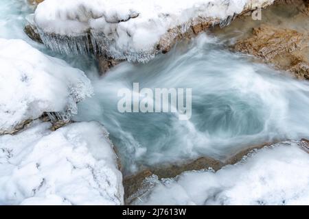 Eiszapfen hängen über dem klaren Wasser des Rissbaches in Tirol an einem schmalen Punkt bei Hinterriss. Stockfoto