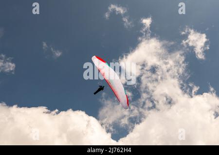 Ein Gleitschirm im blauen und leicht bewölkten Himmel von unten fotografiert Stockfoto