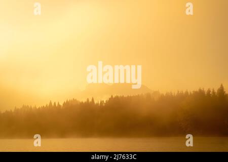 Der Geroldsee, auch Wagenbrüchsee an einem frühen Herbstmorgen. Das Licht des Sonnenaufgangs färbt alles orange-golden, im Hintergrund sieht man den Schatten des Karwendels. Stockfoto