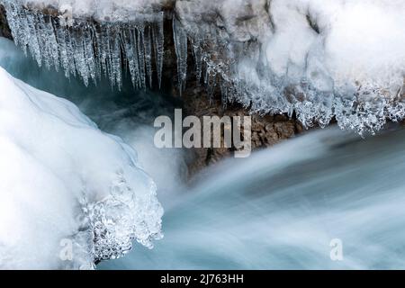 Eiszapfen hängen über dem klaren Wasser des Rissbaches in Tirol an einem schmalen Punkt bei Hinterriss. Stockfoto