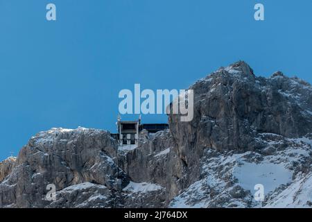 Die Bergstation der Karwendelbahn im Winter mit Schnee, Eis und harten Felsen. Eine Hütte auf dem Weg zum Gebäude. Stockfoto