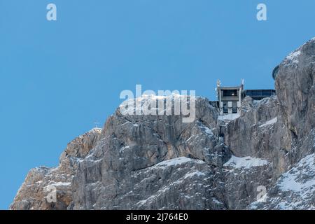 Die Bergstation der Karwendelbahn im Winter mit Schnee, Eis und harten Felsen. Eine Hütte auf dem Weg zum Gebäude. Stockfoto