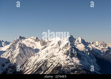 Das Wettersteinmassiv, mit Wetterstein, Zugspitze und den anderen Bergen. Aufgenommen im Winter mit Schnee und blauem Himmel von der Bergstation der Karwendelbahn oberhalb von Mittenwald. Stockfoto