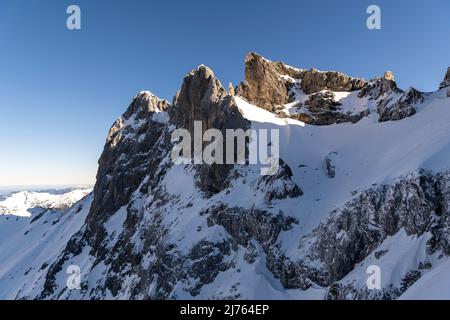 Die Karwendelköpfe Berge oberhalb der Bergstation der Mittenwald Karwendelbahn im Winter mit Schnee. Die schneebedeckten Felsen ragen in den blauen Himmel. Stockfoto