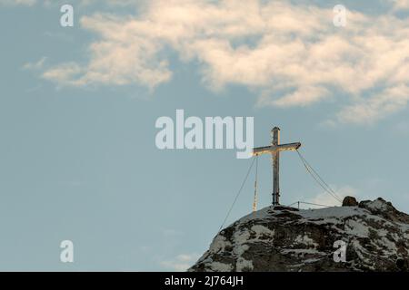 Das eingeschneite Gipfelkreuz der Westlichen Karwendelspitze im Karwendel oberhalb von Mittenwald, nahe der Bergstation der Karwendelbahn. Das Kreuz ist teilweise vereist, im Hintergrund der blaue Himmel. Stockfoto