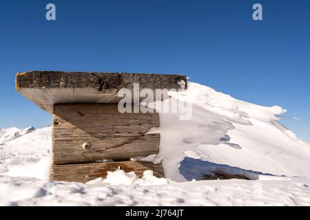 Eine Bank an der Bergstation der Karwendelbahn am Westkarwendel, in Schnee und Eis, mit bizarren Eiszapfen, die horizontal vom Sitz weg gehen. Stockfoto