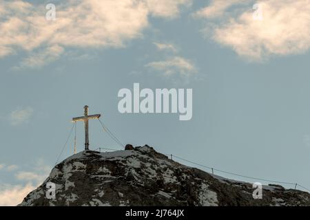 Das eingeschneite Gipfelkreuz der Westlichen Karwendelspitze im Karwendel oberhalb von Mittenwald, nahe der Bergstation der Karwendelbahn. Das Kreuz ist teilweise vereist, im Hintergrund der blaue Himmel. Stockfoto