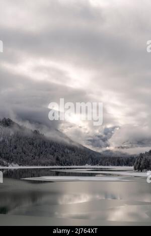 Der Sylvensteinspeichersee am Rande des Karwendelgebirges in den bayerischen Alpen im Winter mit Schnee und teilweise mit Eis, sowie Wolkenatmosphäre. Stockfoto