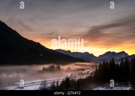 Die Isar windet sich durch die mit Reif bedeckte und im Winter teilweise verschneite Landschaft. Im Hintergrund glühen die Zugspitze und ein fantastischer Abend über den Wettersteingebirge. Stockfoto