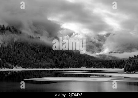 Der Sylvensteinspeichersee am Rande des Karwendelgebirges in den bayerischen Alpen im Winter mit Schnee und teilweise mit Eis, sowie Wolkenatmosphäre. Stockfoto