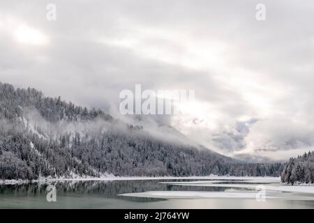 Der Sylvensteinspeichersee am Rande des Karwendelgebirges in den bayerischen Alpen im Winter mit Schnee und teilweise mit Eis, sowie Wolkenatmosphäre. Stockfoto