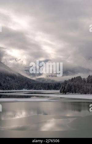 Der Sylvensteinspeichersee am Rande des Karwendelgebirges in den bayerischen Alpen im Winter mit Schnee und teilweise mit Eis, sowie Wolkenatmosphäre. Stockfoto