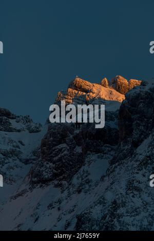 Gipfel der westlichen Karwendelspitze im letzten Abendlicht, unterhalb der Bergstation der Karwendelbahn im Schatten. Im Winter mit Schnee und Eis aufgenommen. Stockfoto