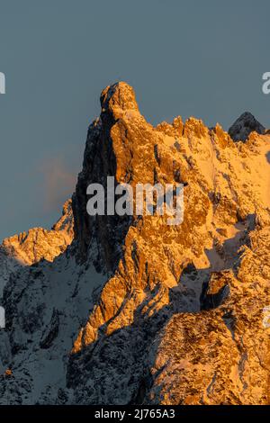 Die Viererspitze (2054 m ü.d.M.) oberhalb von Mittenwald, unterhalb der westlichen Karwendelspitze, als Teil des nördlichen Karwendel-Gebirges im Abendglühen der untergehenden Sonne in roten und orangen Farbtönen gegen einen blauen Himmel im Winter mit Schnee. Stockfoto