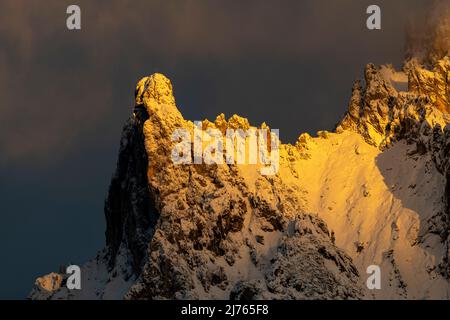 Die Viererspitze (2054 m ü.d.M.) oberhalb von Mittenwald, unterhalb der westlichen Karwendelspitze, als Teil des nördlichen Karwendel-Gebirges im Abendglühen der untergehenden Sonne in roten und orangen Farbtönen gegen einen blauen Himmel im Winter mit Schnee. Stockfoto