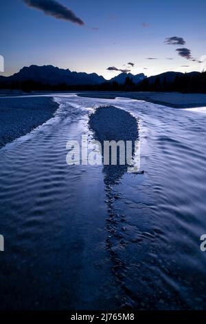 Die Isar im Werdenfelser Land, umgeben von den bayerischen Alpen. Das Abendlicht wird im Wasser reflektiert, das durch das flache Kiesbett mit kleinen Inseln fließt. Stockfoto