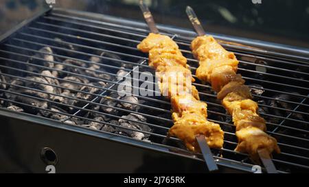 Shashlik – traditionelle georgische Grillspezialitäten. Nahaufnahme von rohem, geröstetem, mariniertem Fleisch Barbecue-Schisch-Kebab-Schaschlik auf Stahlspießen aus Metall, die am Grillfeuer liegen Stockfoto