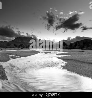 Der Wasserlauf der Isar bei Wallgau kurz nach Sonnenuntergang als Langzeitbelichtung. Im Hintergrund das Wettersteingebirge und die Zugspitze, umhüllt von dichten Wolken. Stockfoto