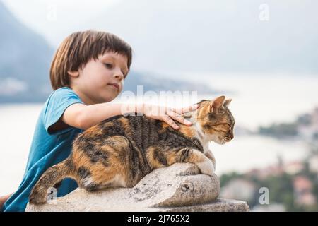 Kind streichelt eine Katze auf der Steinmauer der alten Festung St. Ivan der Altstadt von Kotor und der Bucht von Kotor in Montenegro Stockfoto