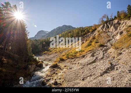 Sonne mit Sonnenstrahlen am herbstlichen Joghannisbach im Johannistal mitten im Karwendel bei Hinterriss. Stockfoto