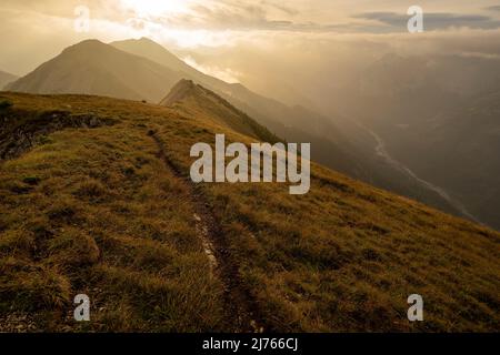 Morgenstimmung mit leichtem Nebel und Wolken an der sogenannten Fleischbank im Karwendel, oberhalb von Hinterriss, in den Tiroler Alpen. Die Hintergrundbeleuchtung der aufgehenden Sonne zeigt harte Schatten und eine fast goldene Stimmung. Stockfoto