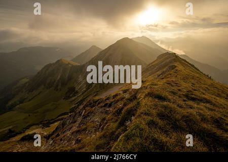 Morgenstimmung mit leichtem Nebel und Wolken an der sogenannten Fleischbank im Karwendel, oberhalb von Hinterriss, in den Tiroler Alpen. Die Hintergrundbeleuchtung der aufgehenden Sonne zeigt harte Schatten und eine fast goldene Stimmung. Stockfoto