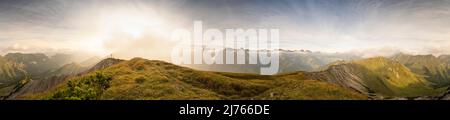 Panoramabild von der sogenannten Fleischbank am frühen Morgen, bei trübendem Wetter und Wolken. Eine Wolke verbirgt die Sonne hinter dem Gipfelkreuz. Stockfoto