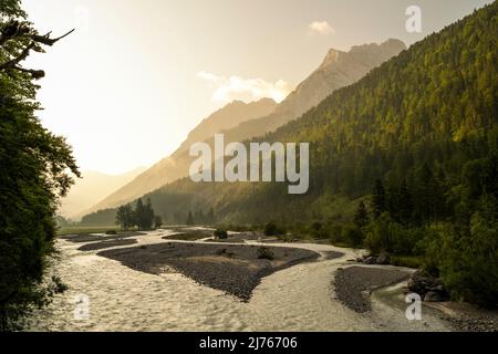 Der Rissbach im engen Tal, nach Hinterriss im Karwendel, Tirol im Morgenlicht mit der aufgehenden Sonne. Der Bach schlängelt sich an einer Wiese vorbei durch die Berge. Im Vordergrund rechts einer der sogenannten Falken, dahinter das Gamsjoch Stockfoto