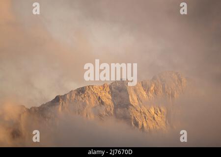 Der Grat der östlichen Karwendelspitze in Karwendel / Tirol zwischen Wolken, fotografiert vom Vorderskopf kurz vor Sonnenuntergang mit einem leichten Alpenglühen. Stockfoto