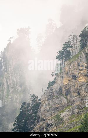 Die Felswände am Herzogstand in den bayerischen Alpen vom Walchensee aus gesehen. Dichter Nebel und Wolken hängen zwischen den zerklüfteten Felsen. Stockfoto