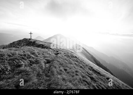 Der Gipfel der Fleischbank im Karwendel mit seinen klassischen Bergwiesen im Spätsommer bei Sonnenaufgang mit dichten Wolken und Nebel, im Hintergrund der Kompar und andere Gipfel der österreichischen Alpen. Stockfoto