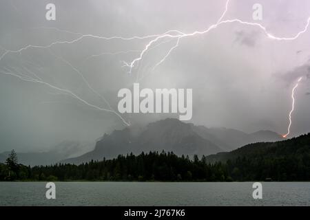 Gewitterblitz am Karwendel oberhalb von Mittenwald in die westliche Karwendelspitze. Im Vordergrund der Lautersee und der Wald. Stockfoto