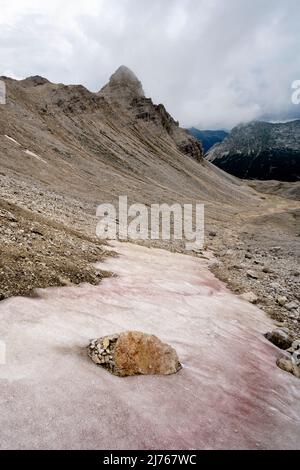 Im Hochgebirge der alpinen Hinterau-Vomper-Gebirgskette in Karwendel bleibt Staub und Sand der roten Sahara auf dem Schnee. Im Hintergrund die unwirtliche Landschaft und dichte Wolken. Stockfoto